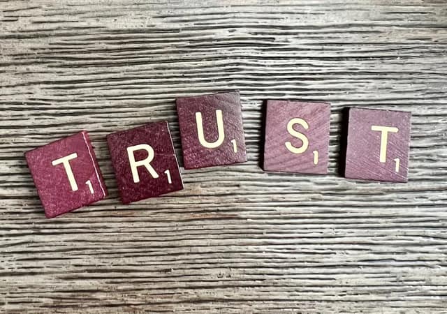Wooden Scrabble tiles spelling the word TRUST on weathered wood